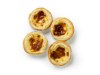 Quatre tartes Pastel de Nata dorées avec des dessus caramélisés dans des moules en aluminium.