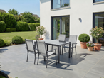 Conjunto de jantar exterior com mesa e cadeiras num pátio junto a uma casa moderna.