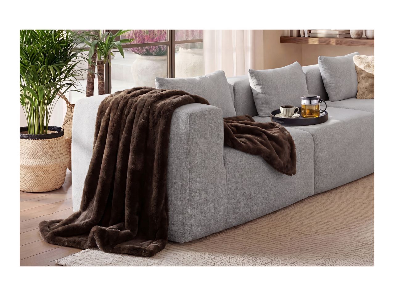 Cozy brown faux fur blanket draped over a modern grey sofa with a tea tray.