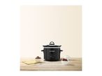 Black slow cooker on a wooden table with two bowls of food and a yellow napkin.