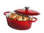 Red oval cast iron pot with a lid, filled with roasted meat, tomatoes, and herbs.
