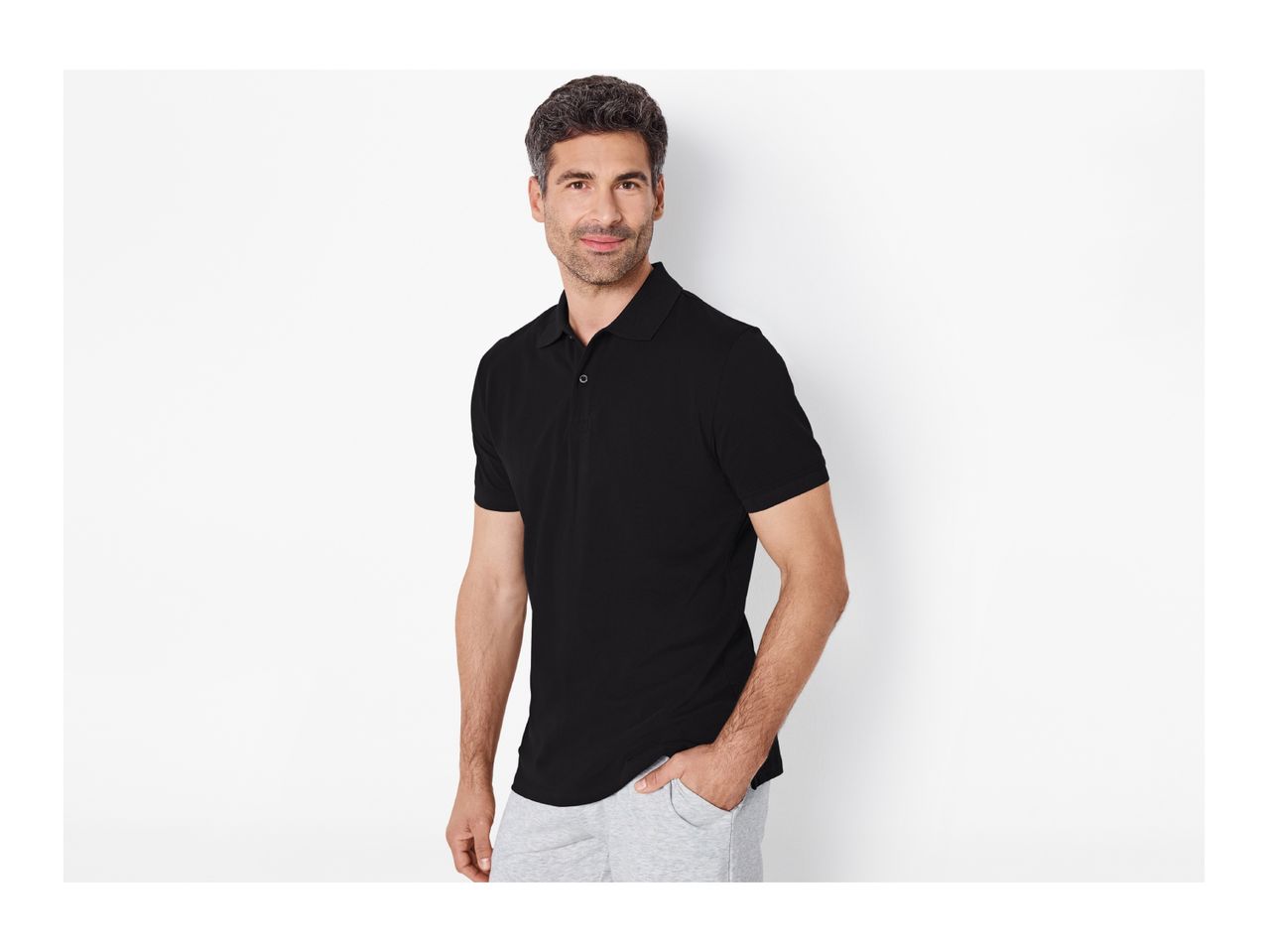 Man in black polo shirt and grey sweatpants, smiling at the camera.