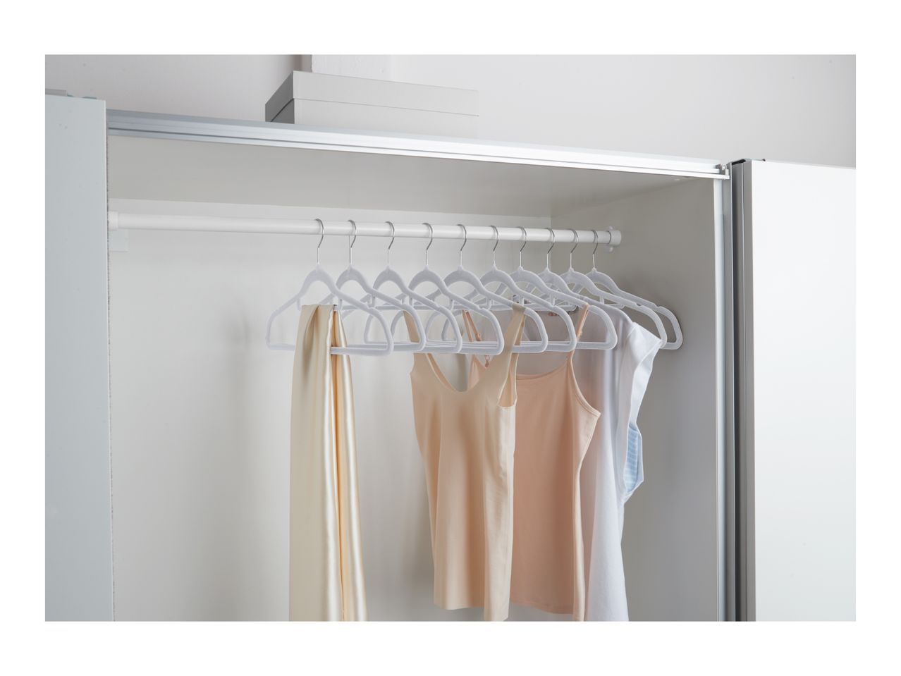 White velvet hangers with various tops and a scarf hanging in a closet.