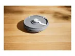 A gray plastic lid with a white stirring attachment on a wooden surface.