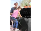 A man and a girl looking into a black outdoor storage box with potted plants on top.