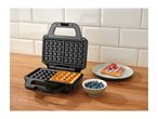 Waffle maker with a freshly made waffle, blueberries, and a waffle with strawberries.