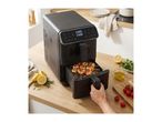 Black air fryer with chicken and vegetable skewers, lemons, and herbs on a wooden counter.