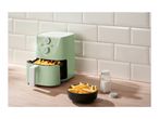 A light green air fryer with fries inside and a bowl of fries next to it on a wooden counter.