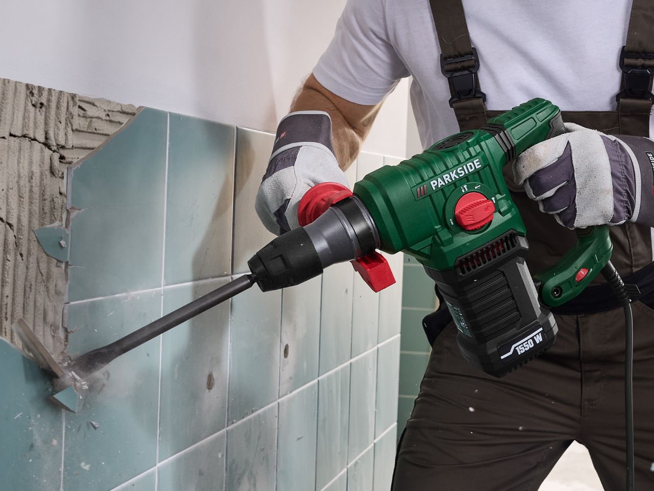 Person using a demolition hammer to remove light blue tiles from a wall.