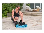 Man in athletic wear folding a blue and black inflatable lounge chair outdoors.