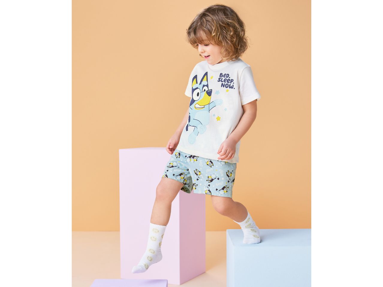 Toddler boy in white short-sleeved pajamas with a blue dog print and text 