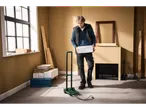Man holding a box, standing next to a hand truck in a room under renovation.