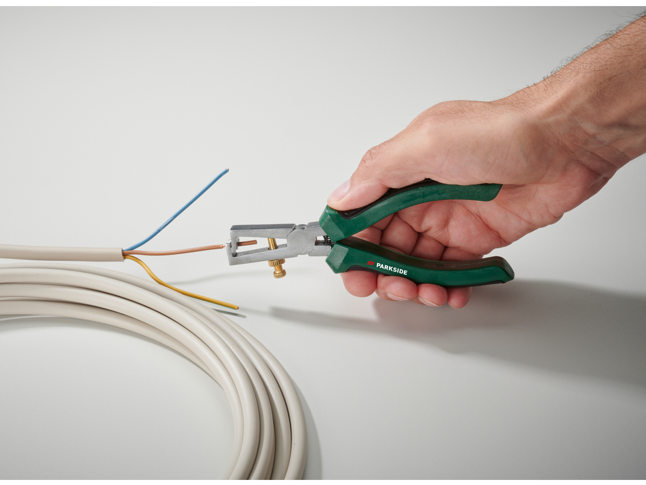 Hand using a Parkside wire stripper to remove insulation from a cable.