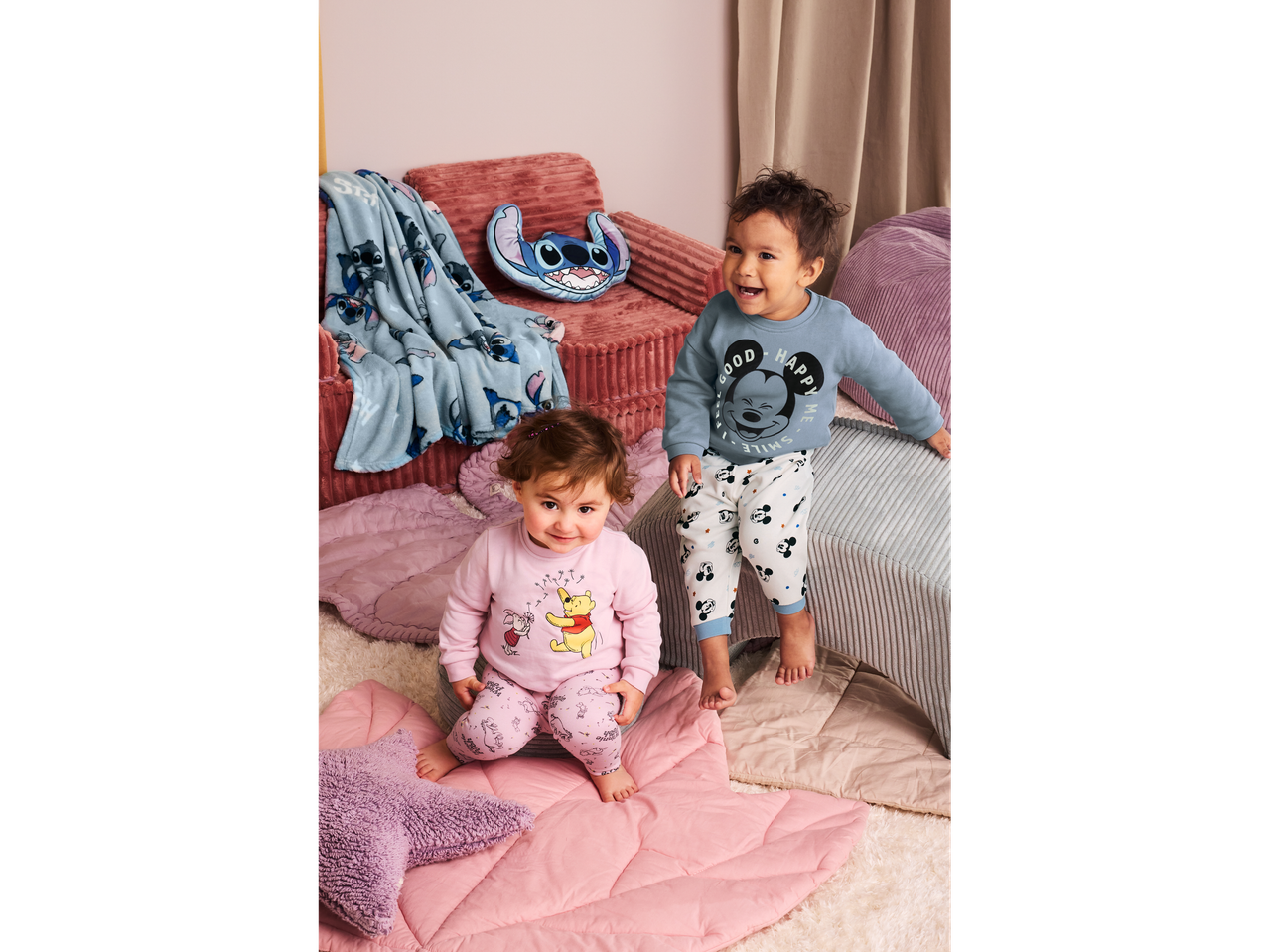 Doi copii mici în pijamale cu personaje Disney, înconjurați de o pătură și o pernă Stitch.