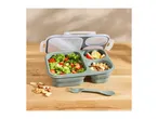 Lunchbox with salad, apple slices, nuts, and a spork on a wooden table.