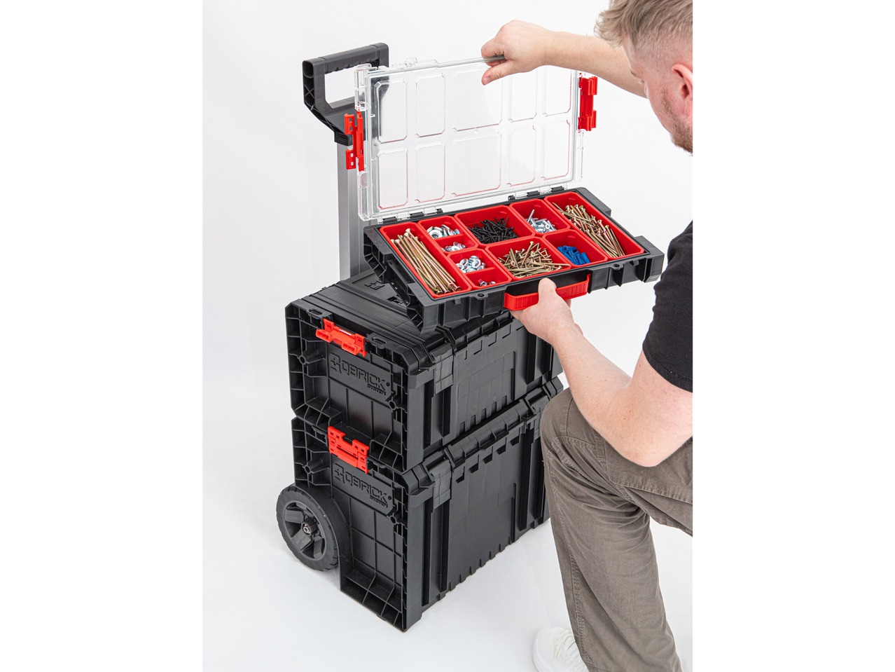 Un homme soulève un bac à outils Qbrick System avec des tiroirs transparents remplis de vis et de boulons.