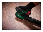 A person sanding a wooden floor with a power sander connected to a dust extraction hose.