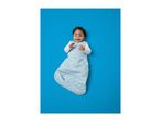Happy baby in a light blue sleep sack with polka dots, lying on a blue background.