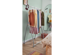 Roupas em um cabideiro com rodinhas em um quarto: tops, calças e jaquetas.