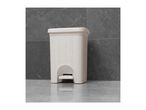 White rattan-style pedal bin on a grey tiled floor against a grey tiled wall.