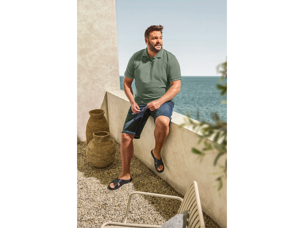 LIVERGY Herren Pantolette Sandalen, Poloshirt und Jeans-Shorts, Mann sitzt am Meer