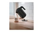 Black electric kettle pouring hot water into a mug on a wooden countertop.