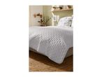 A light gray quilted bedspread on a bed with patterned pillows in a bedroom.