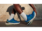 Pessoa com sapatilhas de corrida Crivit azuis e meias brancas, alongando-se contra uma parede.