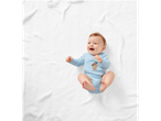 Happy baby in a blue bodysuit with an acorn graphic, lying on a white blanket.