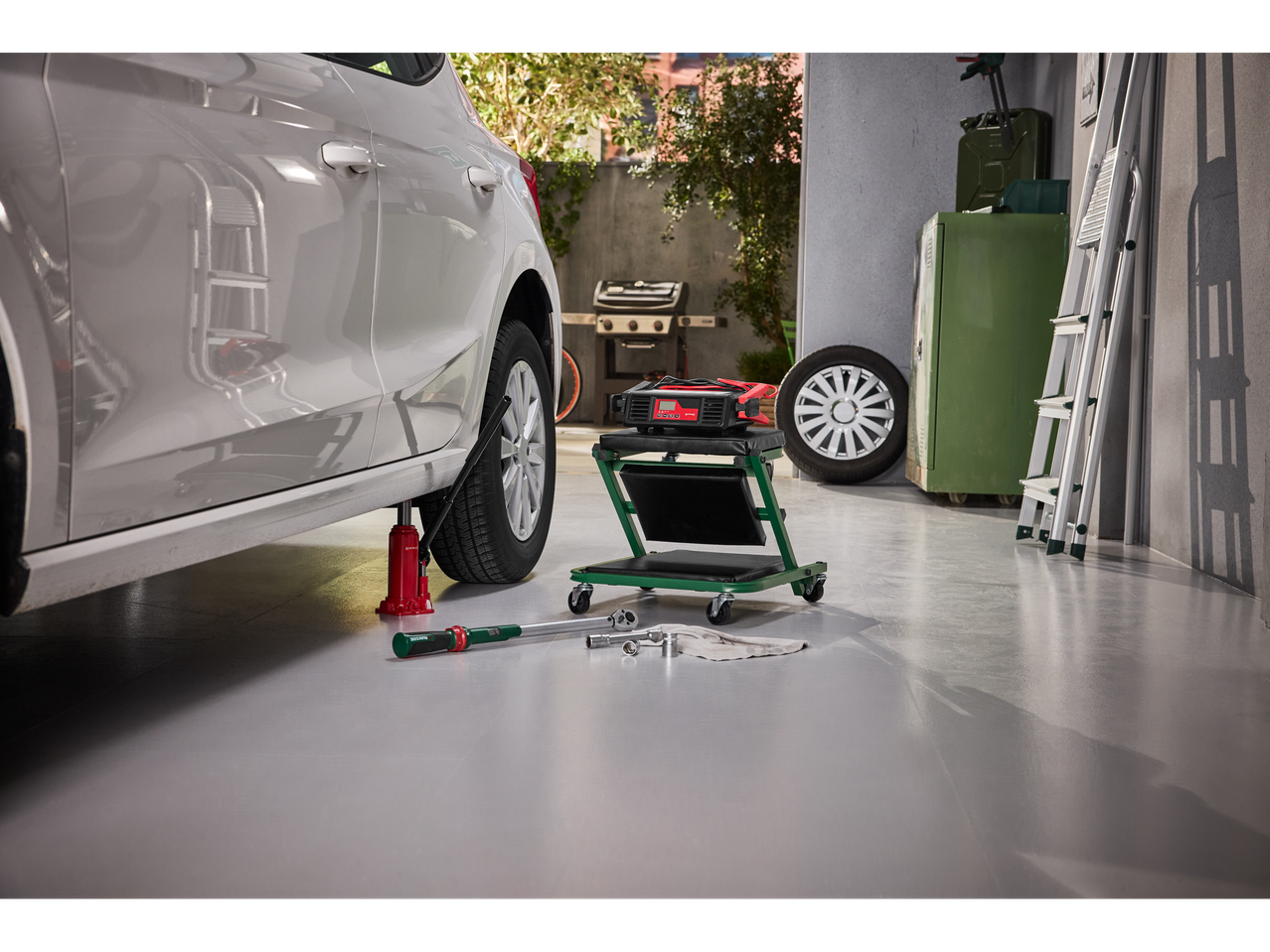 Încărcător de baterie Ultimate Speed® pe un scaun de atelier rulant, lângă o mașină ridicată.