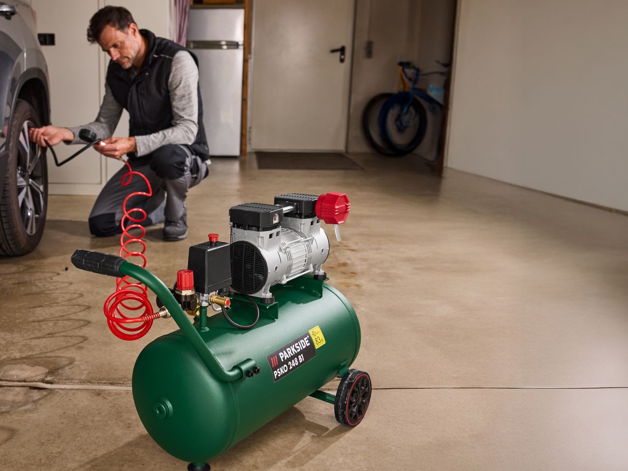 Un uomo gonfia il pneumatico di un'auto con un compressore d'aria Parkside verde in un garage.