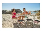 Couple enjoying a beach picnic with a folding table, chairs, and a water bottle.