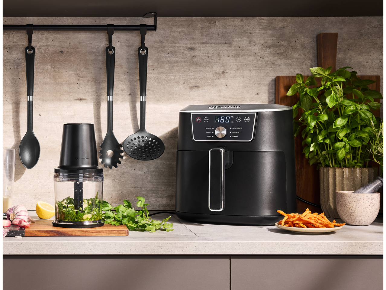 A SILVERCREST® XL Air Fryer on a kitchen counter with cooking utensils and fresh ingredients.
