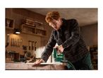 Man in safety glasses and earplugs using a jigsaw to cut wood in a workshop.