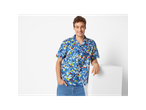 Man wearing a blue pixelated Lidl short sleeve shirt and jeans, smiling.
