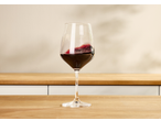 Copo de vinho tinto em movimento sobre uma mesa de madeira, com fundo claro