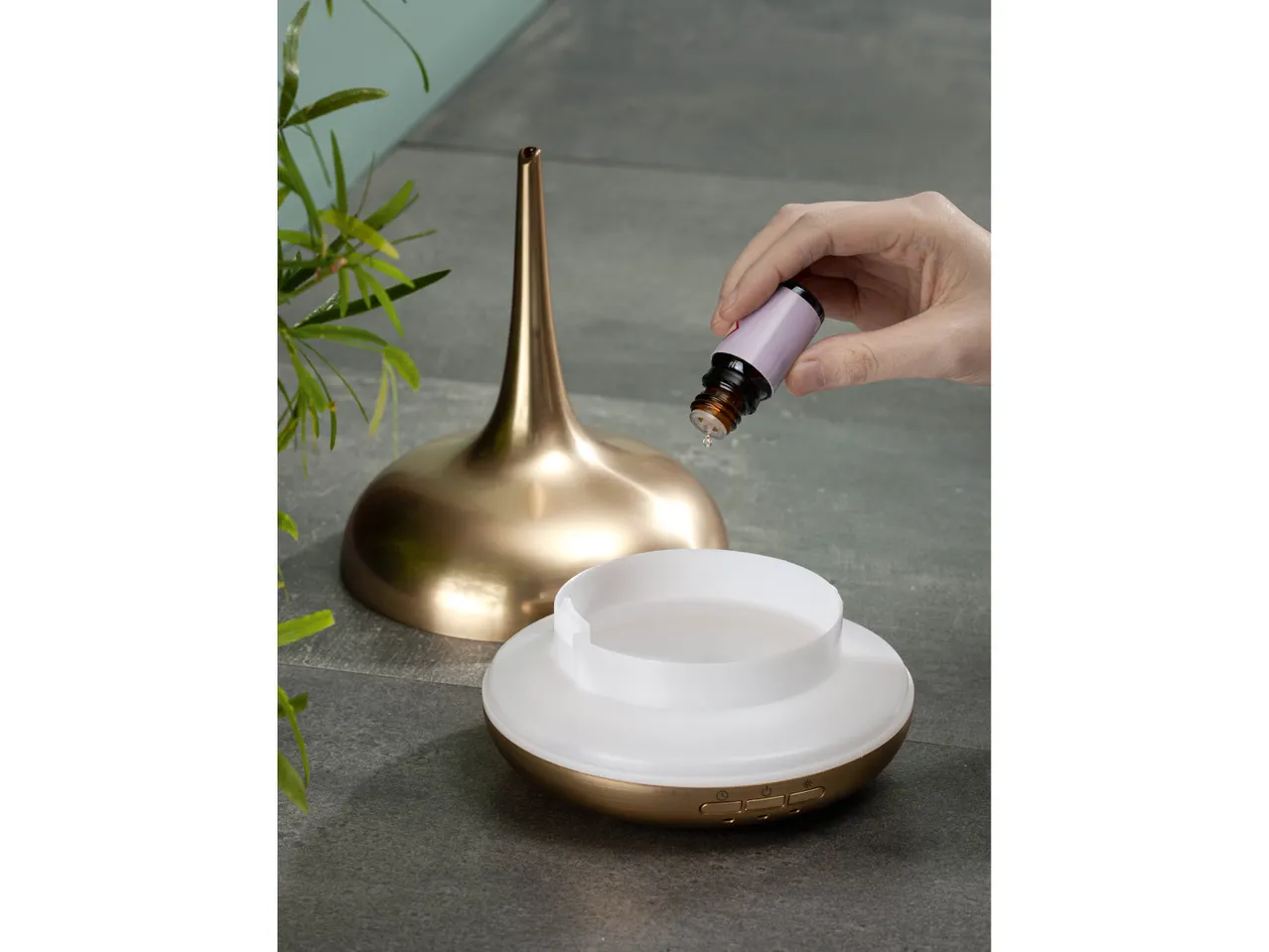 Mano che aggiunge olio essenziale a un diffusore d'aromi dorato.