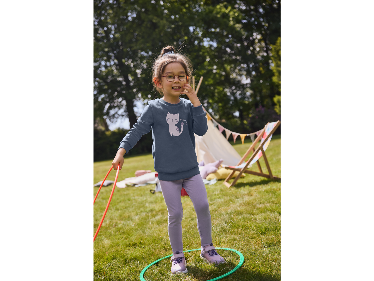 Fată cu ochelari jucându-se cu cerc hula hoop în grădină.
