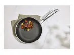 Frying pan with a cooked steak and vegetables on a light marble surface.