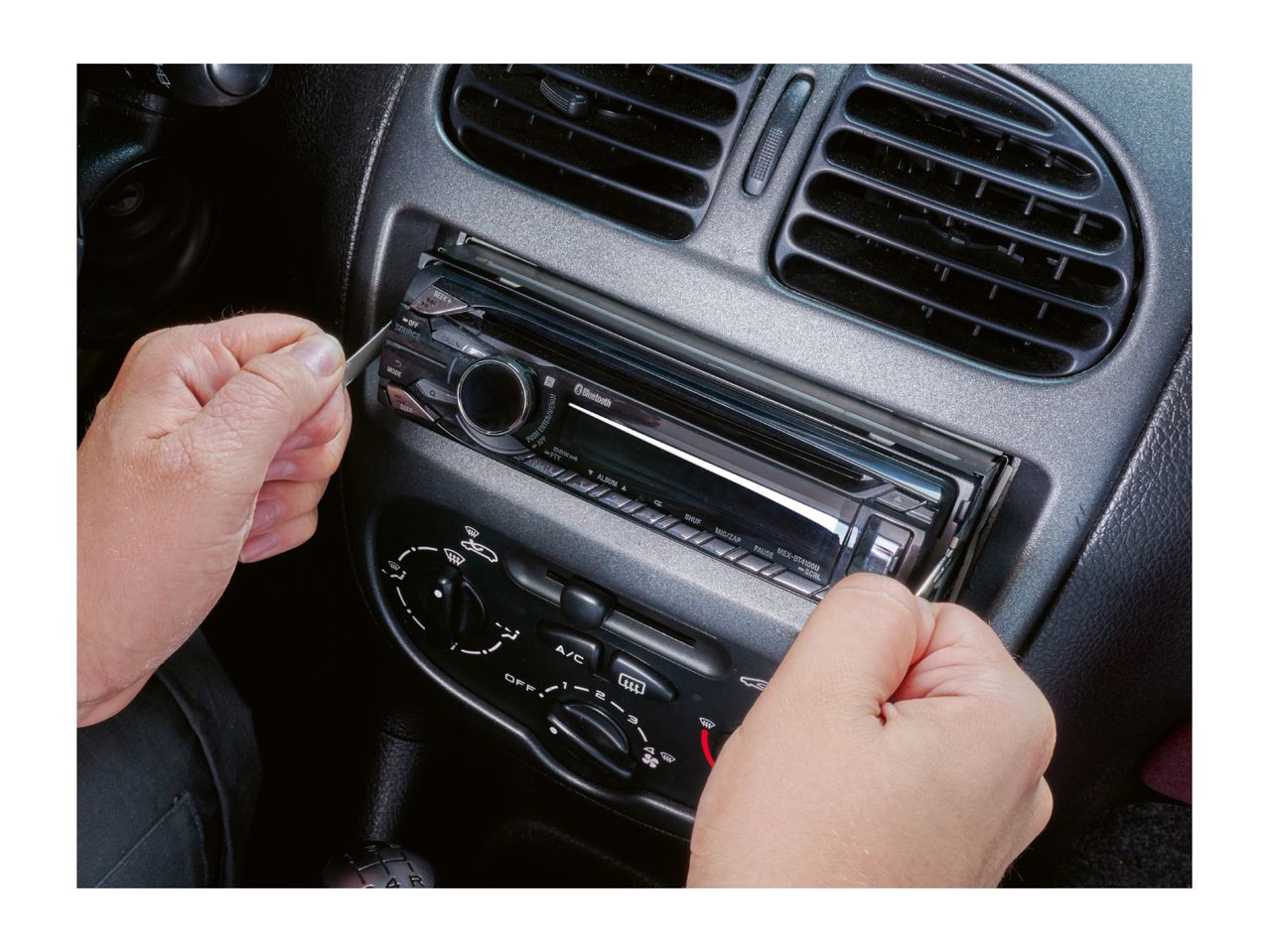 A person using release keys to remove a car stereo from a vehicle dashboard.