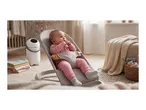 Baby in a bouncer, with a diaper pail and stacked baby blankets nearby.