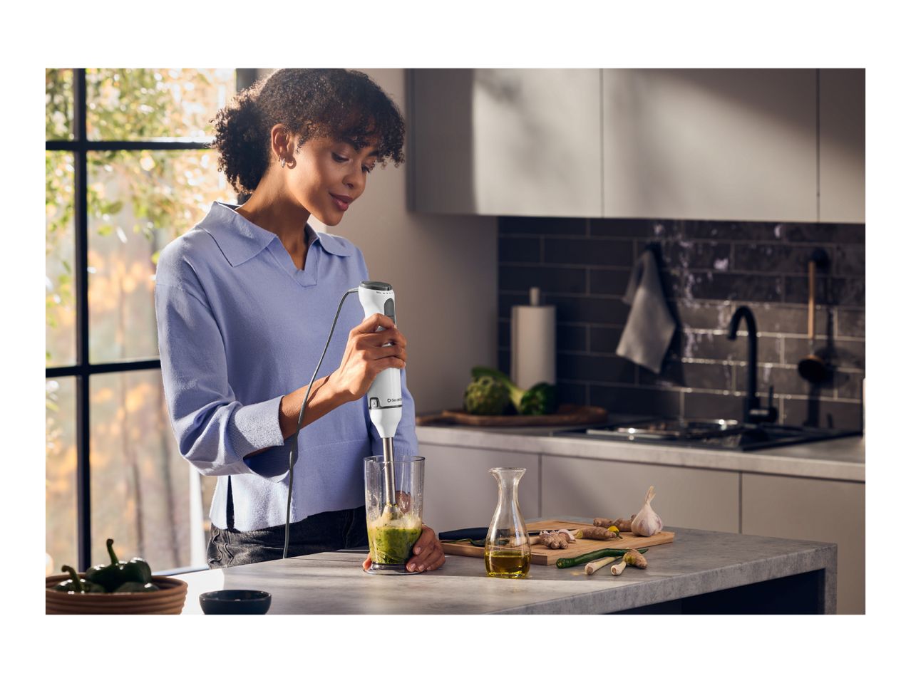 A woman uses a hand blender to mix ingredients in a kitchen.