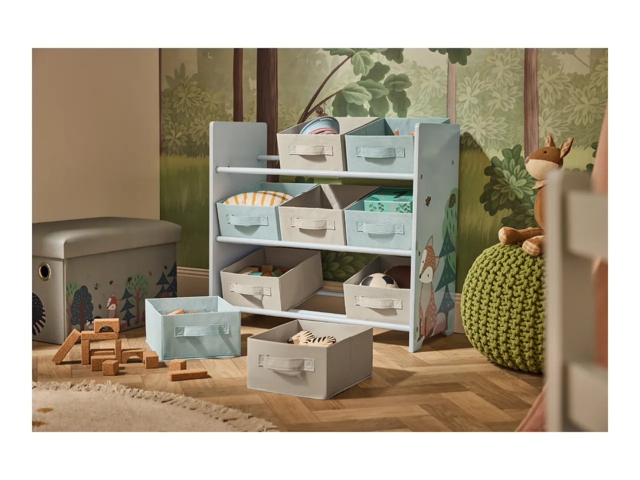 A child's room with a forest-themed wallpaper, a toy storage unit, and a storage ottoman.