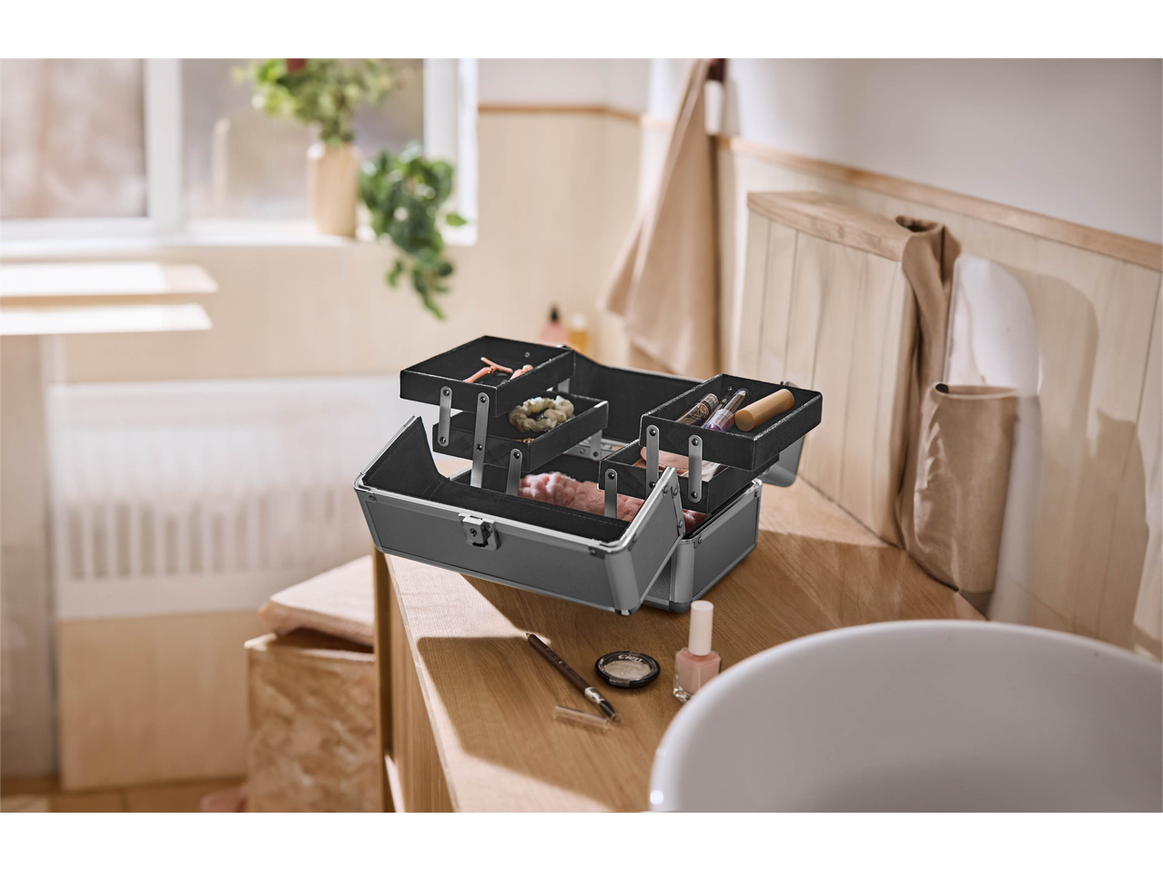 Open makeup case with cosmetics and hair accessories on a wooden bathroom counter.