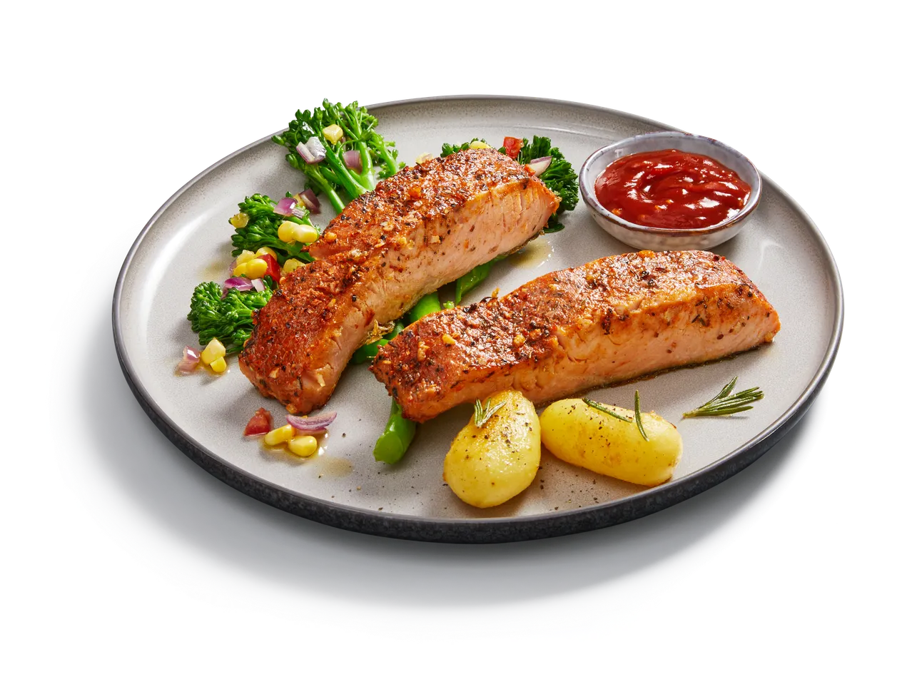Zwei gegrillte Lachsfilets mit Bratkartoffeln, Brokkoli und Mais, dazu eine kleine Schale Ketchup.