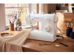 Singer Tradition sewing machine on a wooden table with fabric and sewing accessories.
