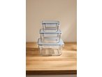 Stack of three rectangular glass food storage containers with light blue lids on a wooden surface.