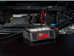 Car battery charger connected to a car engine, with the hood open.