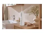 White oral irrigator on a wooden bathroom counter with a sink and flowers in the background.