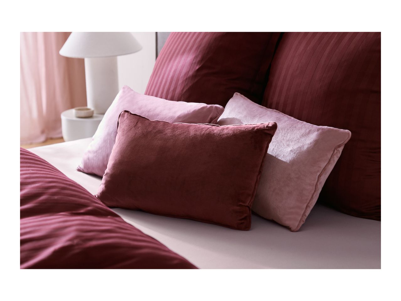 Plush decorative pillows in shades of pink and burgundy on a bed.